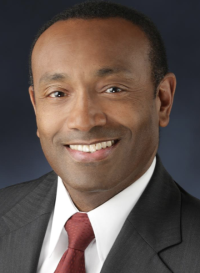 Headshot of man in suit and tie. He is smiling.